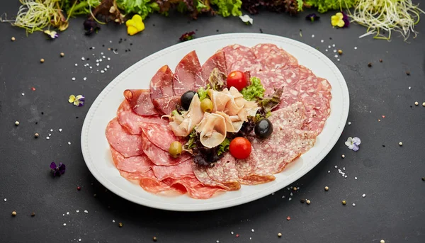 Soğuk et tabağı, jambon, sosis, salam, parma, prosciutto, koyu arkaplanda salam ve zeytin ile kesilmiş domuz pastırması. Et aperatifi, şarap seti, yakın çekim.