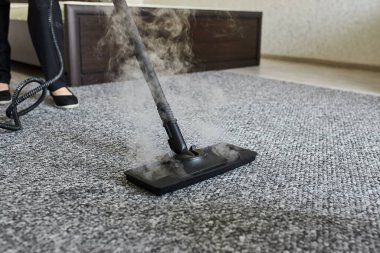 Temizlik şirketi çalışanı, profesyonel buhar temizleme ekipmanıyla halıdaki kiri temizliyor.