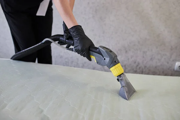 Cleaning service company employee removing dirt from furniture in flat with professional equipment. Female housekeeper arm cleaning the mattress on the bed with washing vacuum cleaner close up