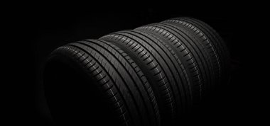 Yeni araba lastikleri. Karanlık arka planda bir grup yol tekeri. Asimetrik lastik dizaynlı yaz lastikleri. Araba sürme kavramı.