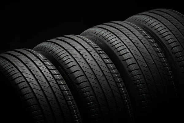 Yeni araba lastikleri. Karanlık arka planda bir grup yol tekeri. Asimetrik lastik dizaynlı yaz lastikleri. Araba sürme kavramı.