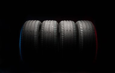 Yeni araba lastikleri. Karanlık arka planda bir grup yol tekeri. Asimetrik lastik dizaynlı yaz lastikleri. Araba sürme kavramı.