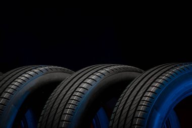 Yeni araba lastikleri. Karanlık arka planda bir grup yol tekeri. Asimetrik lastik dizaynlı yaz lastikleri. Araba sürme kavramı.