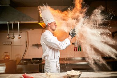 Profesyonel pasta şefi ekmek, İtalyan makarnası ya da pizza yapmak için hamur ve un hazırlar. Un, mutfak arka planında havada uçuşuyor. Yemek pişirme kavramı