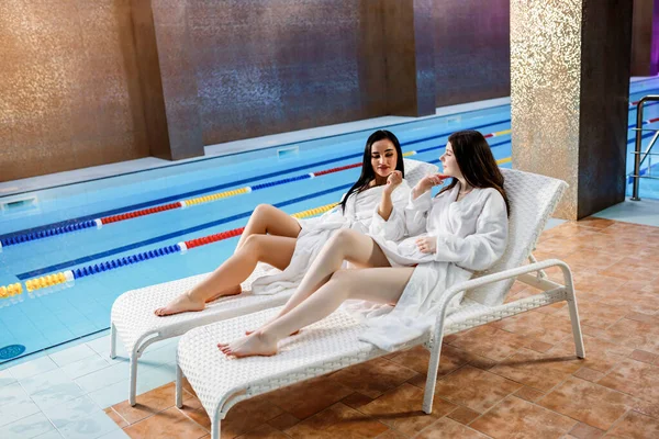 健康的生活方式的概念 身穿浴衣的年轻漂亮姑娘们在游泳池边的甲板椅子上的豪华温泉里放松一下 健康主题 — 图库照片