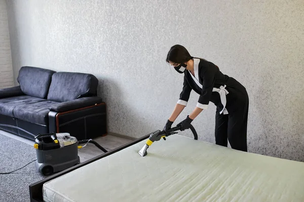 Cleaning service company employee removing dirt from furniture in flat with professional equipment. Woman housewife cleaning the mattress on the bed with a washing vacuum cleaner