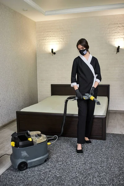 Portrait of Cleaning service company employee removing dirt from furniture in flat with professional equipment. Woman housewife cleaning the mattress on the bed with a washing vacuum cleaner