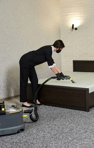 Cleaning company employees remove dirt from furniture in the apartment using professional equipment. Housewife women cleaning the mattress and floor with washing and steam vacuum cleaners