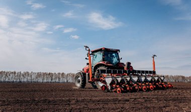 Vinnitsa, Ukraine - April 20, 2022: Spring sowing season. Farmer with a tractor sows corn seeds on his field. Planting corn with trailed planter. Farming seeding