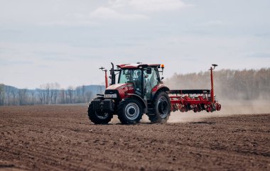 Vinnitsa, Ukraine - April 20, 2022: Spring sowing season. Farmer with a tractor sows corn seeds on his field. Planting corn with trailed planter. Farming seeding