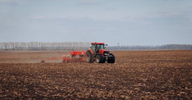 Vinnitsa, Ukraine - April 20, 2022: Spring sowing season. Farmer with a tractor sows corn seeds on his field. Planting corn with trailed planter. Farming seeding