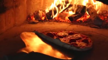 Şef margarita pizzasını kürekle odun fırınına koyuyor. 