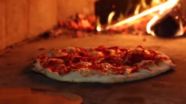 Pizzaiolo margarita pizzasını ahşap fırına koyuyor.