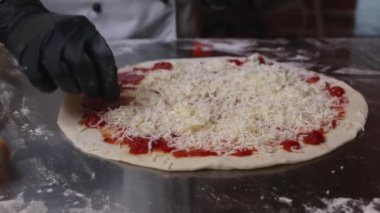 Geleneksel bir pizzacı mutfağında peynire domates sosu sürüyor. Kapat.