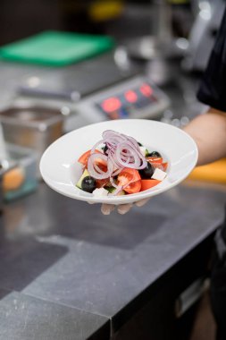 Taze hazırlanmış Yunan salatasını beyaz tabakta tutuyor. Vejetaryen salatası arayışı.