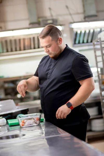 Şef tavuk leşine baharat serpiyor ve marine etmek için hazırlıyor.