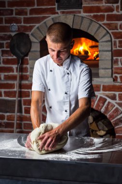 Şef, mutfakta odun yakan fırının yanında İtalyan pizzası pişirmek için hamuru masanda yoğurur.