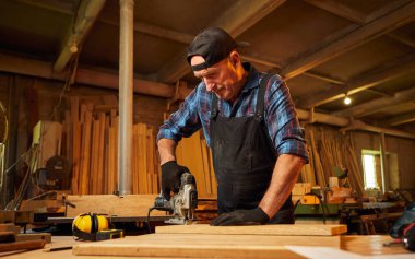 Kıdemli profesyonel marangoz marangozluk atölyesinde elektrikli testereyle odun kesiyor.