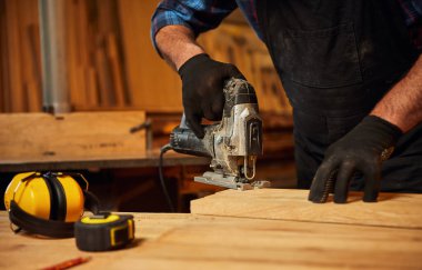 Close up of professional carpenter hands sawing wood with an electric jigsaw in the carpentry workshop