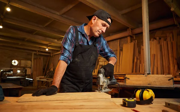Kıdemli profesyonel marangoz marangozluk atölyesinde elektrikli testereyle odun kesiyor.