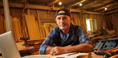 Gülümseyen marangoz portresi atölyedeki bilgisayarda çalışır.