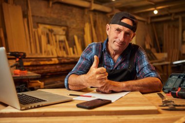 Gülümseyen marangoz portresi bilgisayarda çalışır ve atölyede parmağını kaldırır.