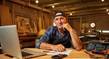 Gülümseyen marangoz portresi atölyedeki bilgisayarda çalışır.