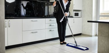 Profesyonel temizlik şirketi çalışanı lastik eldivenli bir paspas ile mutfak zeminindeki kiri temizler, dezenfekte eder ve sterilize eder.