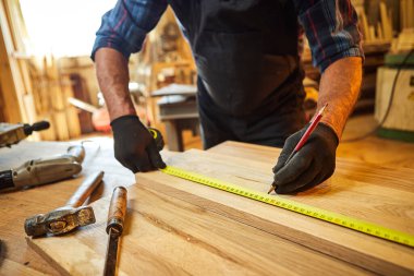 Marangoz bir ahşap ile çalışır, bir kalemle tahta işaretler ve ölçümler yapar bir marangoz atölyesinde bir parça mobilya yapmak için bir parça odun kesmek için, yakın görüş