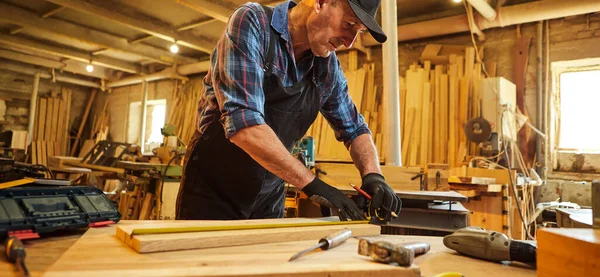 Bir ahşap ile çalışan usta bir marangozun portresi, bir kalemle tahta işaretleme ve marangozluk atölyesinde bir parça mobilya yapmak için bir parça odun kesmek için ölçümler alma