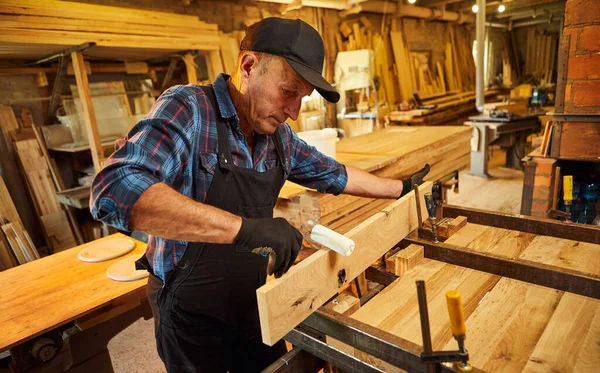 Üniformalı bir marangozun portresi marangozluk fabrikasında ahşap parmaklıkları el baskısıyla yapıştırıyor.