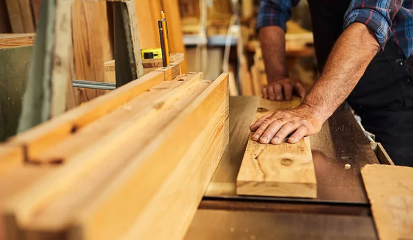 Senior carpenter in uniform works on a woodworking machine at the carpentry manufacturing