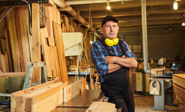 Portrait of Senior carpenter in uniform works on a woodworking machine at the carpentry manufacturing