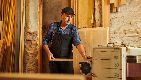 Üniformalı kıdemli marangoz marangozluk fabrikasında ahşap işçiliği yapıyor. 