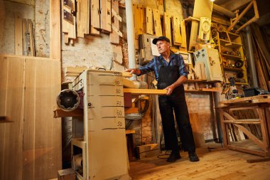 Üniformalı kıdemli marangoz marangozluk fabrikasında ahşap işçiliği yapıyor. 