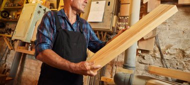 Üniformalı kıdemli marangoz marangozluk fabrikasında ahşap işçiliği yapıyor.