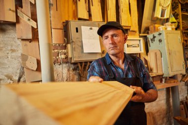 Üniformalı kıdemli marangoz marangozluk fabrikasında ahşap işçiliği yapıyor.