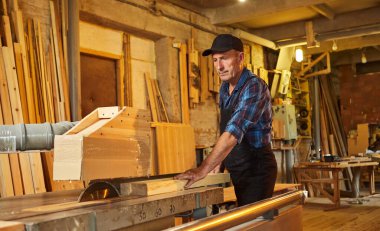 Elektrikli testere ile ahşap kesme masası. Kıdemli profesyonel marangoz üniformalı kereste fabrikasında ahşap tahta kesiyor. Testere makinesi