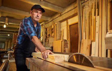 Elektrikli testere ile ahşap kesme masası. Kıdemli profesyonel marangoz üniformalı kereste fabrikasında ahşap tahta kesiyor. Testere makinesi