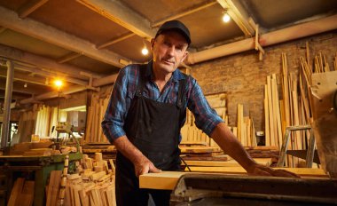 Elektrikli testere ile ahşap kesme masası. Kıdemli profesyonel marangoz üniformalı kereste fabrikasında ahşap tahta kesiyor. Testere makinesi