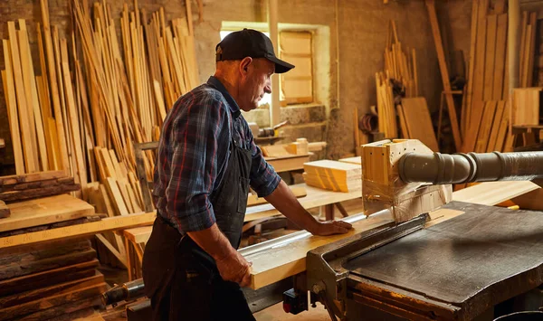 Elektrikli testere ile ahşap kesme masası. Kıdemli profesyonel marangoz üniformalı kereste fabrikasında ahşap tahta kesiyor. Testere makinesi