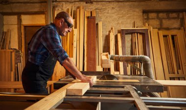 Elektrikli testere ile ahşap kesme masası. Kıdemli profesyonel marangoz üniformalı kereste fabrikasında ahşap tahta kesiyor. Testere makinesi