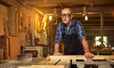 Elektrikli testere ile ahşap kesme masası. Kıdemli profesyonel marangoz üniformalı kereste fabrikasında ahşap tahta kesiyor. Testere makinesi