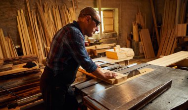 Elektrikli testere ile ahşap kesme masası. Kıdemli profesyonel marangoz üniformalı kereste fabrikasında ahşap tahta kesiyor. Testere makinesi