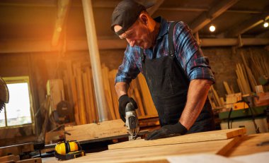 Kıdemli profesyonel marangoz marangozluk atölyesinde elektrikli testereyle odun kesiyor.