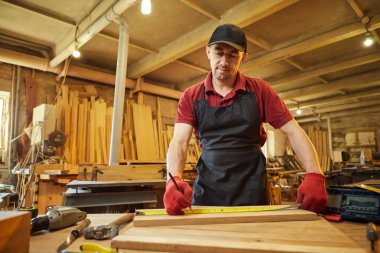 Marangoz bir ahşap ile çalışır, bir kalemle tahta işaretler ve bir marangoz atölyesinde mobilya yapmak için bir parça odun kesmek için ölçümler alır.