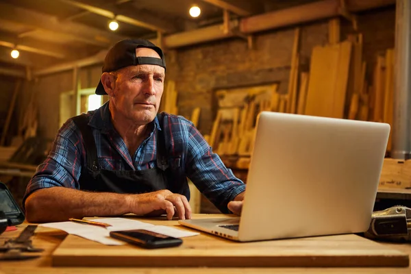 Senior carpenter works on the computer in the workshop