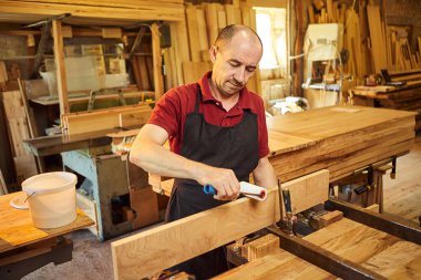 Üniformalı bir marangozun portresi marangozluk fabrikasında ahşap parmaklıkları el baskısıyla yapıştırıyor.