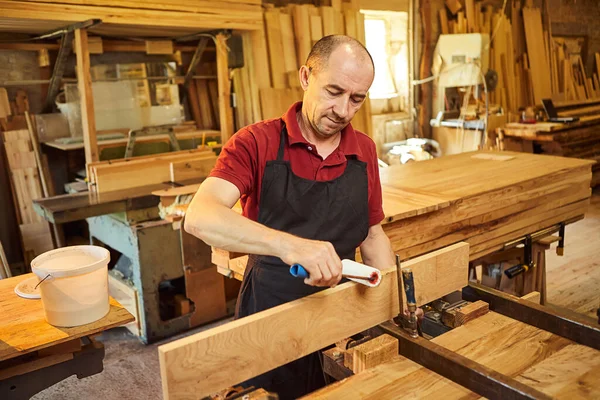 Üniformalı bir marangozun portresi marangozluk fabrikasında ahşap parmaklıkları el baskısıyla yapıştırıyor.