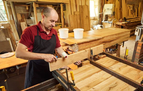 Üniformalı bir marangozun portresi marangozluk fabrikasında ahşap parmaklıkları el baskısıyla yapıştırıyor.